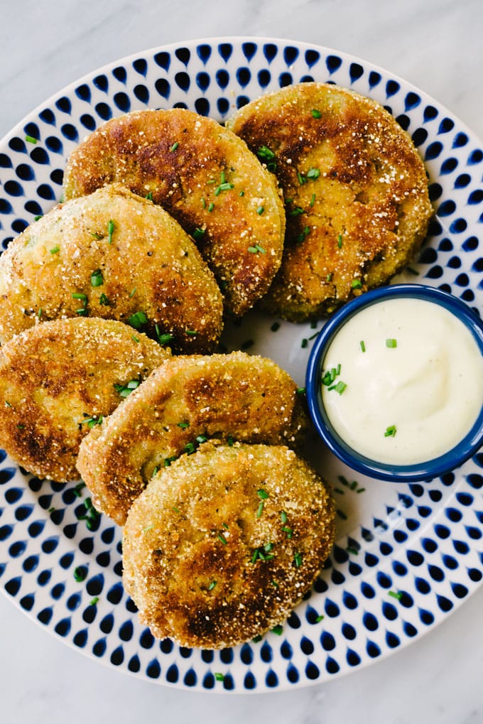 A plate of gluten free fried green tomatoes with a cornmeal crust, served with a small cup of garlic aioli dipping sauce.