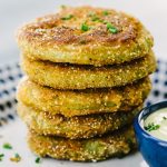 A stack of fried green tomatoes battered in cornmeal, oat flour, and buttermilk with a side of dipping sauce.