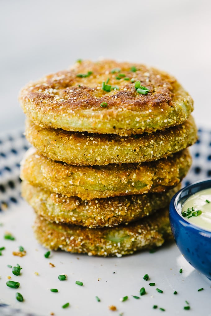 A stack of fried green tomatoes battered in cornmeal, oat flour, and buttermilk with a side of dipping sauce.