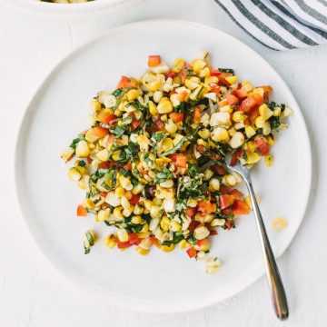 A plate with a serving of grilled corn salad with basil, bell peppers, and lime dressing.