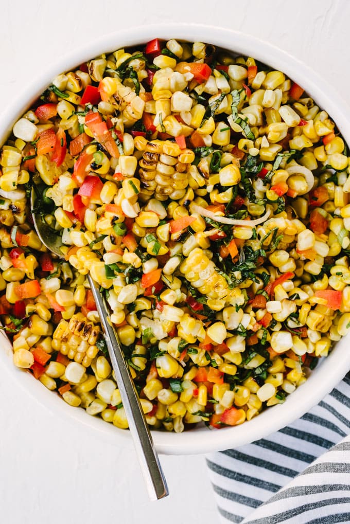 A bowl of grilled sweet corn summer salad with red bell pepper, basil, and green onions and lime honey dressing.