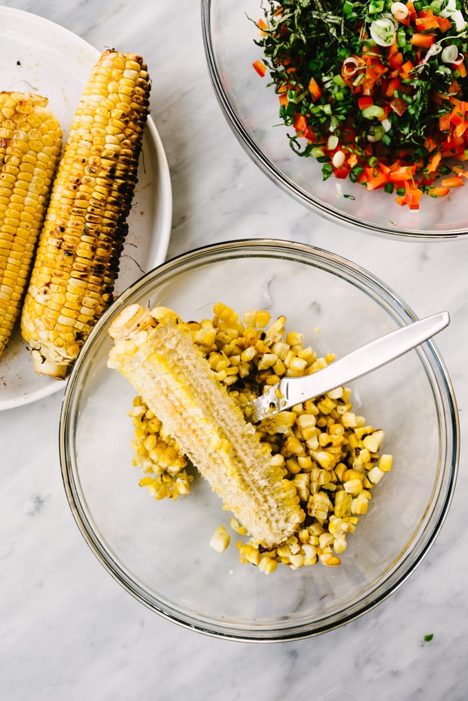 An ear of corn with kernels sliced from the cob in a glass bowl on a marble table.