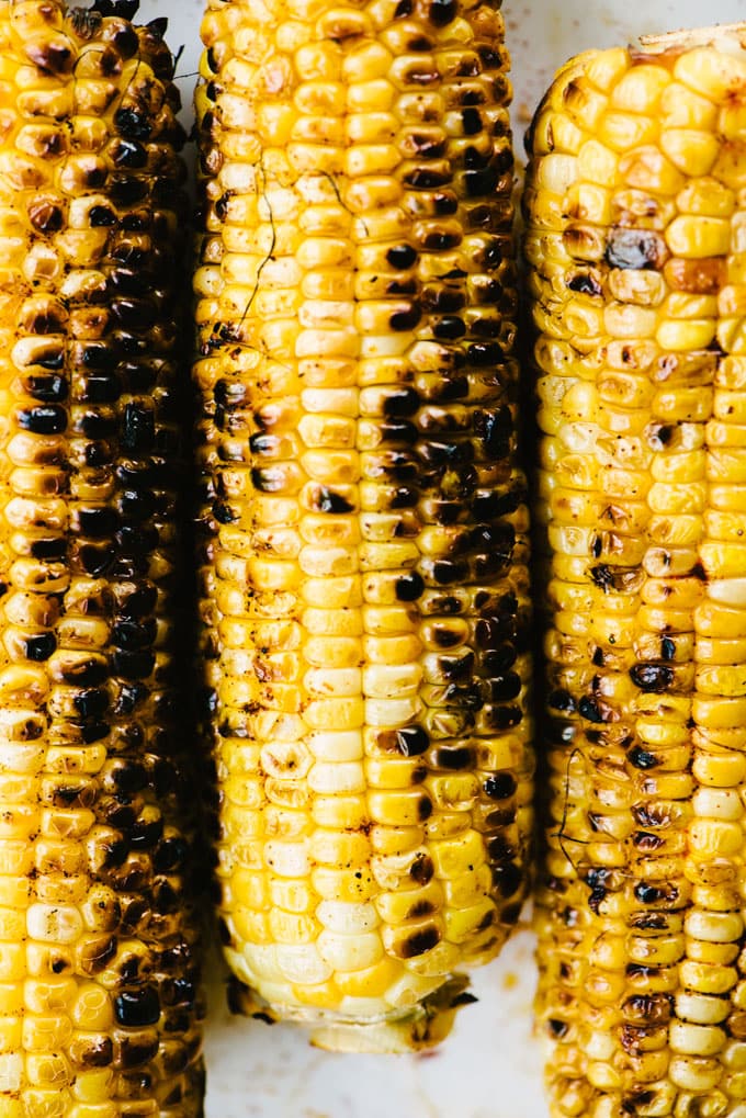 Three ears of charred and grilled sweet corn.