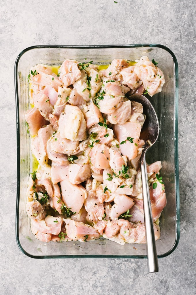 Boneless skinless chicken thigh cut into cubes and tossed with lemon thyme marinade in a glass container.