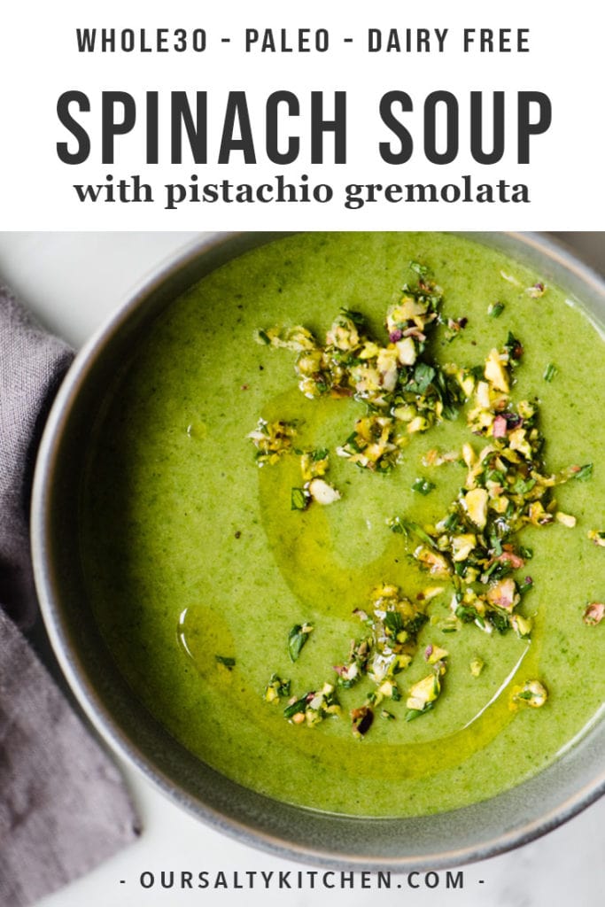 A grey bowl filled with potato spinach green soup, garnished with pistachio gremolata, on a marble table.