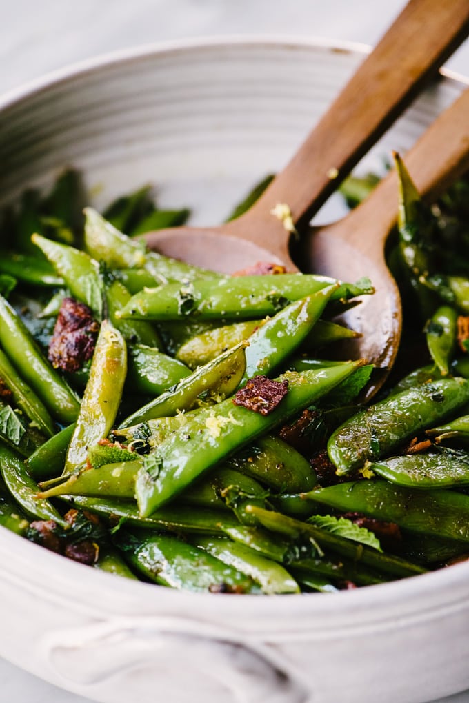 A large serving bowl of sugar snap peas sautéed with bacon and mint.