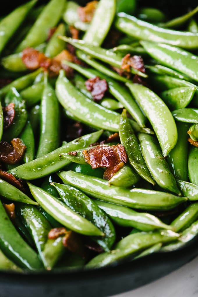 Sugar snap peas sautéed with bacon in a cast iron skillet.