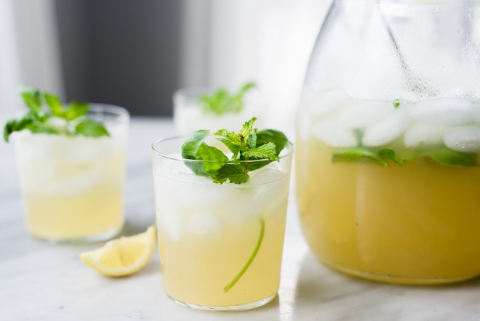 A pitcher of mint and basil lemonade with three glasses filled and garnished with fresh herbs.