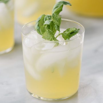 A glass of refreshing, paleo mint and basil lemonade made with honey and garnished with fresh herbs.
