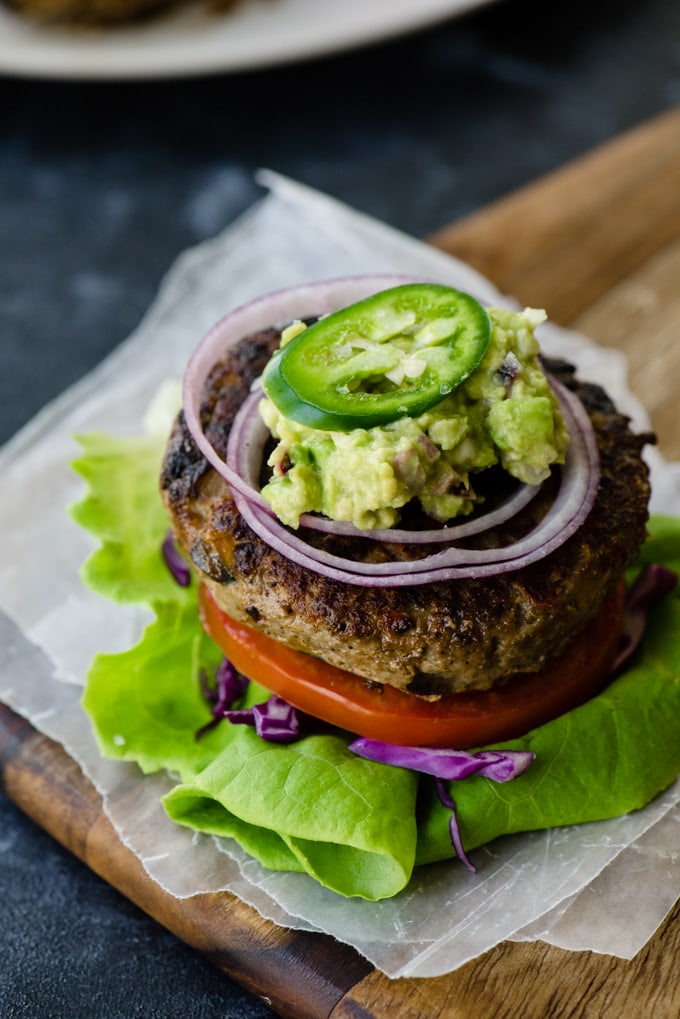 A low carb keto burger on a lettuce and tomato "bun" topped with guacamole and jalapeno.