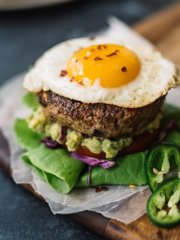 Keto and paleo turkey burger on a bed of lettuce, onion, and tomato with a serving of guacamole and topped with a fried egg.