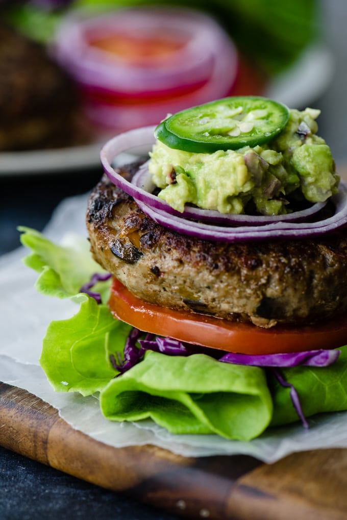A paleo turkey burger served on a lettuce bun with tomato and red onion, topped with guacamole and jalapeno peppers.