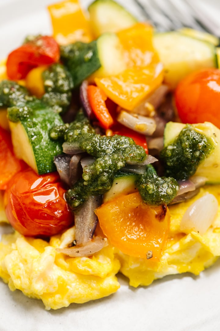 Side view, scrambled eggs with pesto and roasted vegetables on a ceramic plate.
