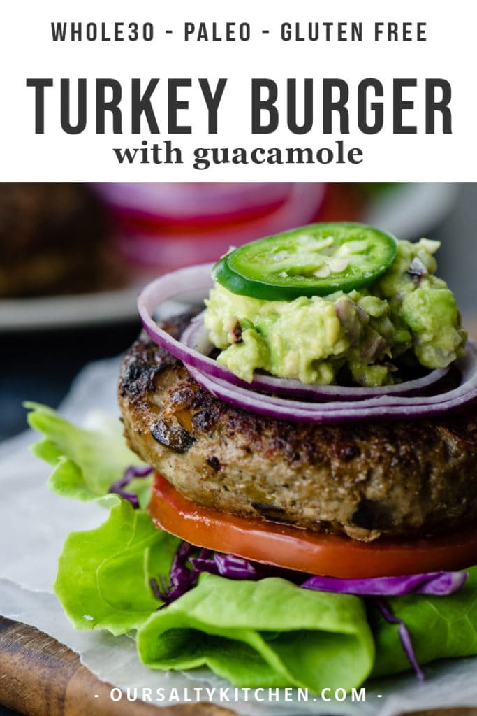 A veggie-packed paleo turkey burger on a lettuce bun with tomato, red onion, and guacamole.