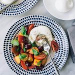 A serving of stone fruit salad with tomatoes and burrata cheese on a blue and white plate.