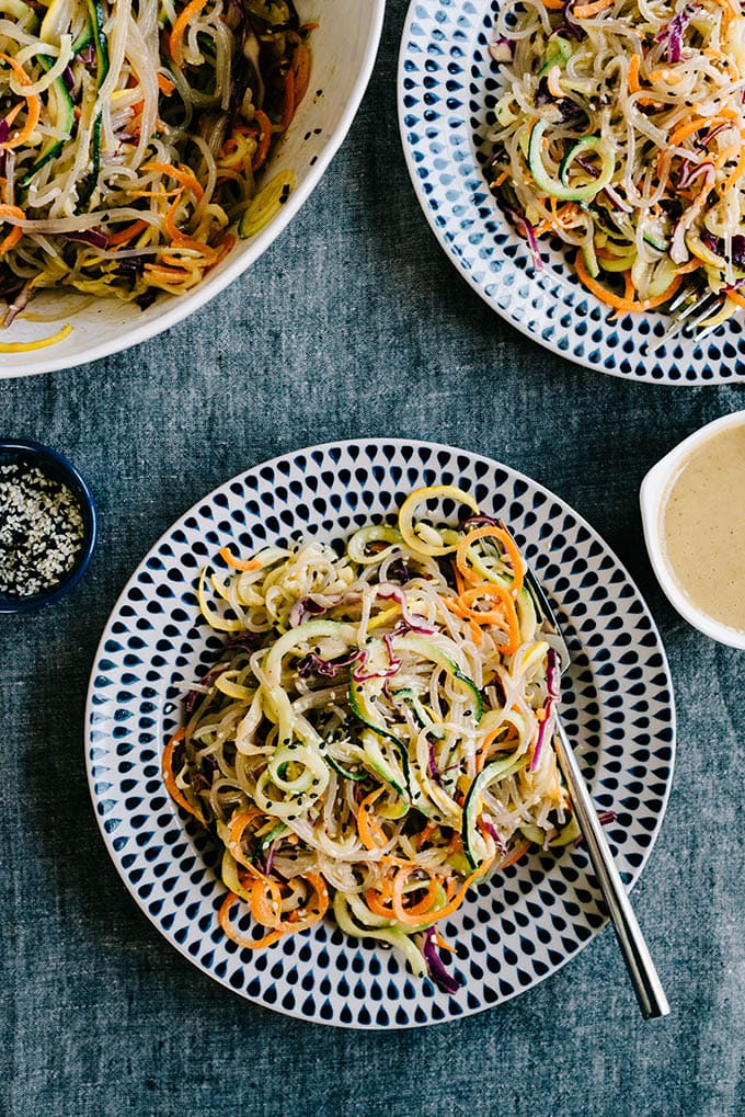 Two plates of sweet potato glass noodle salad tossed with sesame ginger vinaigrette on a grey tablecloth.