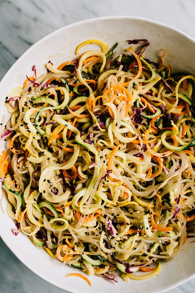 A large white bowl filled with glass noodle salad tossed with paleo sesame ginger dressing and sesame seeds.