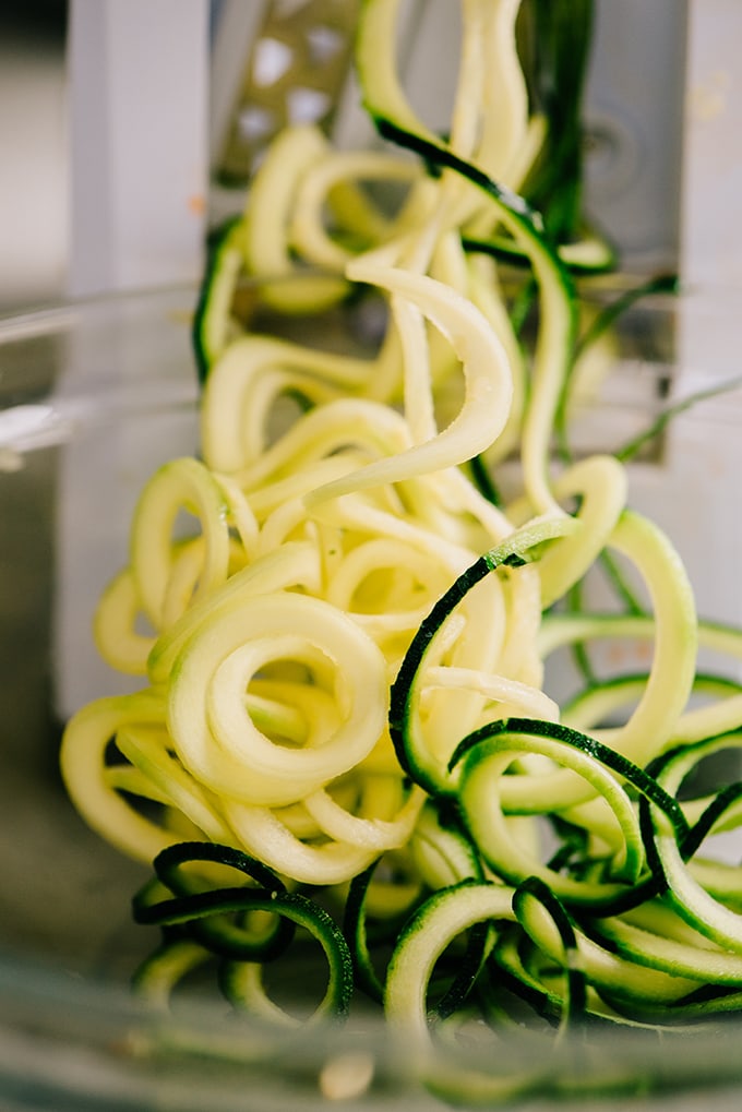 Zucchini being spiralized into a glass bowl.