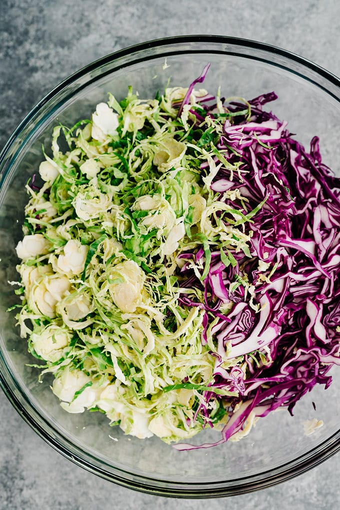 Shredded cabbage and shredded brussels sprouts in a large glass mixing bowl.