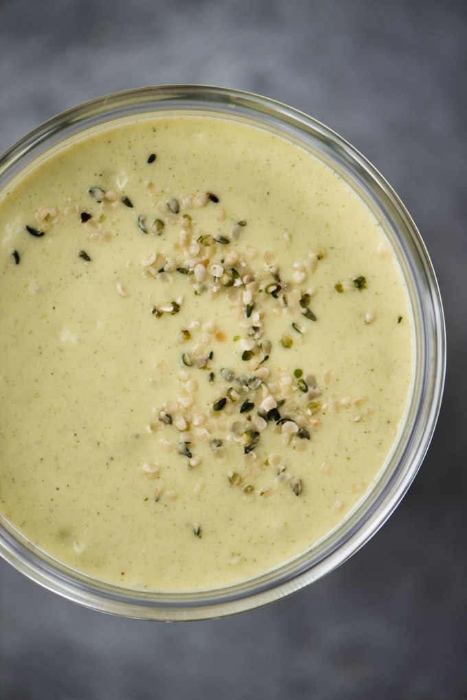 A glass filled with a protein packed mango avocado smoothie sprinkled with hemp seeds. 