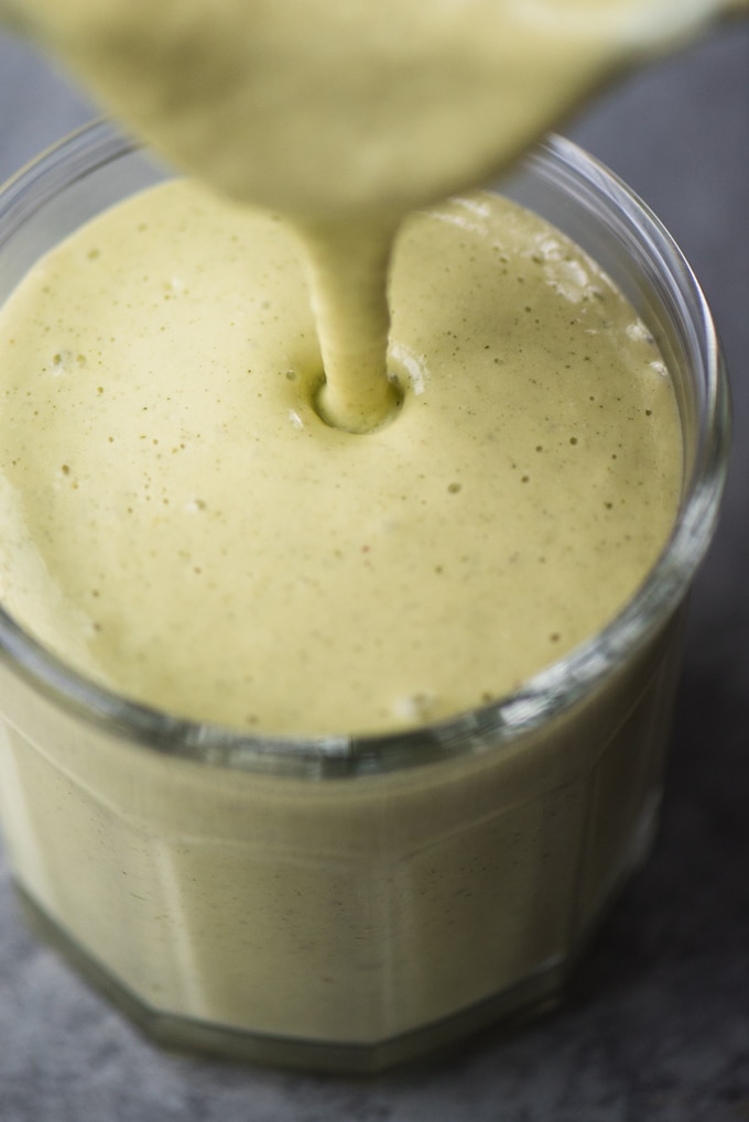Pouring a mango avocado smoothie with protein packed hemp seeds and cashew milk into a glass.