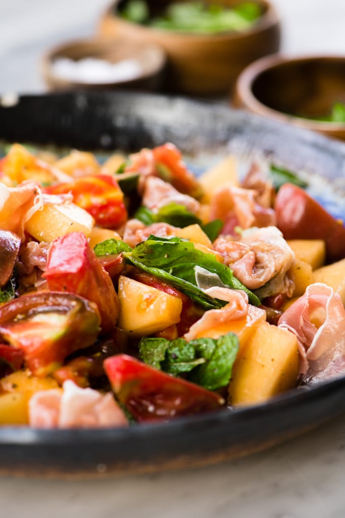 Melon salad with mint, basil, tomato and prosciutto in a blue salad bowl.