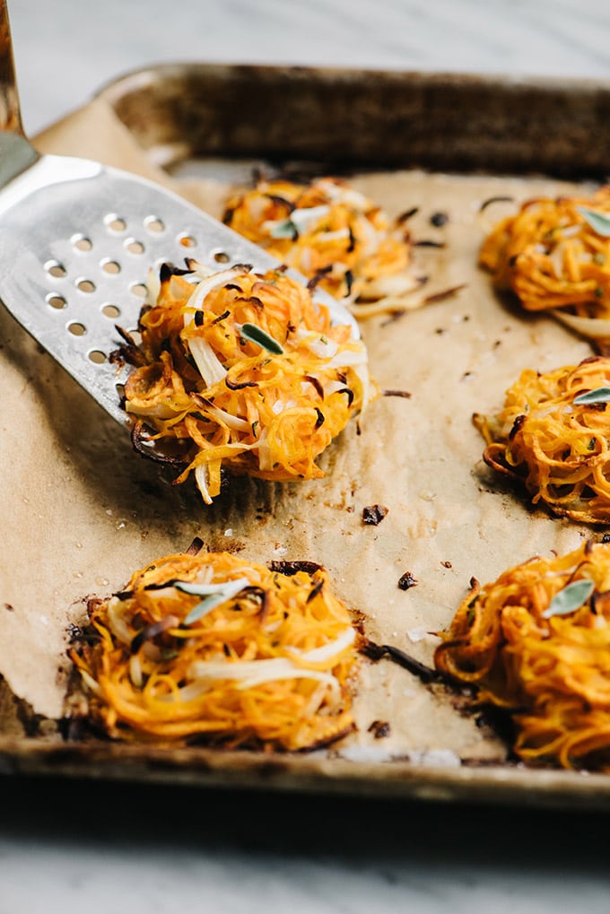 A baking sheet filled with butternut squash and sweet potato fritters with a spatula removing one fritter.