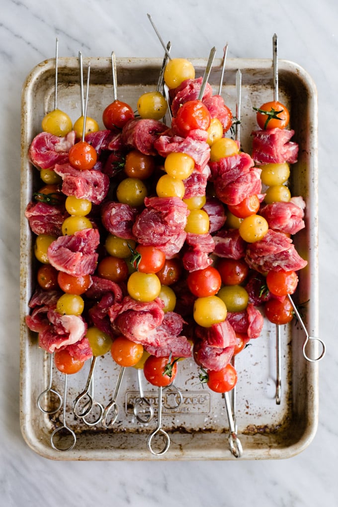 Salt tenderized flank steak threaded onto metal skewers with cherry tomatoes.