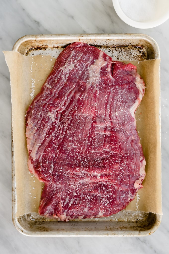 A raw piece of flank steak sprinkled with salt to tenderize.