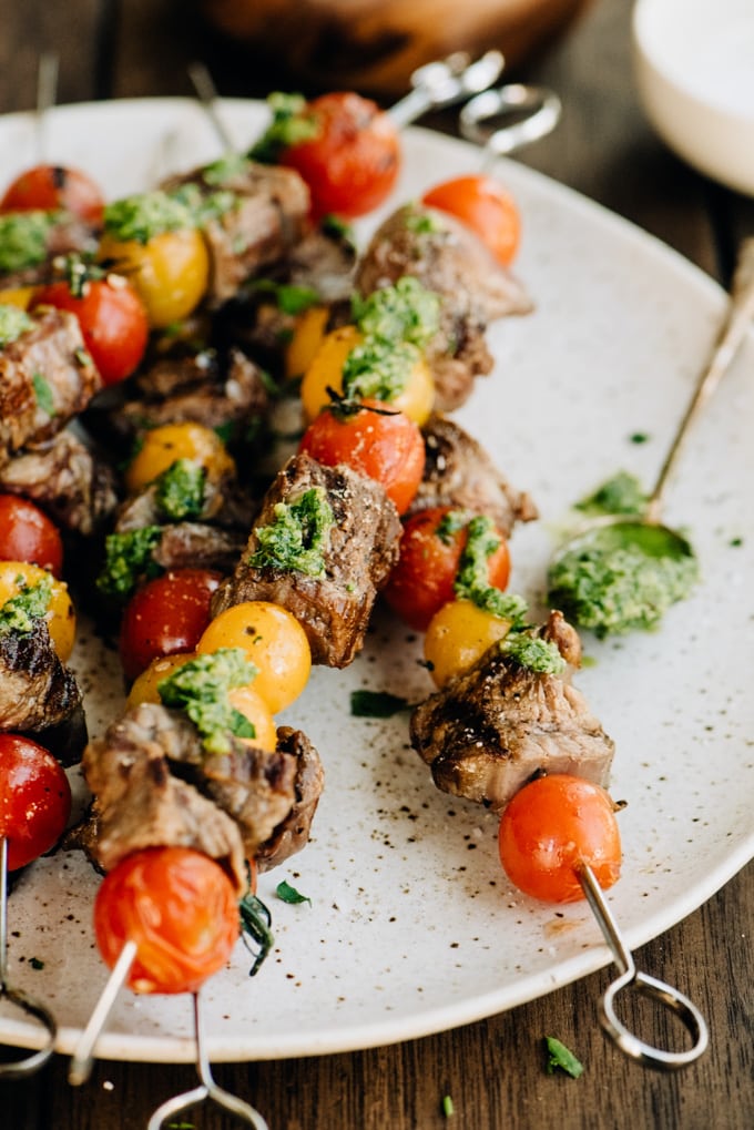 Tomato and flank steak skewers drizzled with dairy free pesto on a wood background.