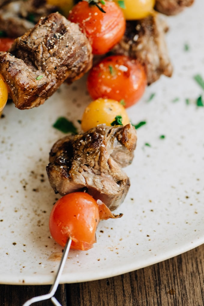 Close-up detail of a grilled steak skewer with burst tomatoes.