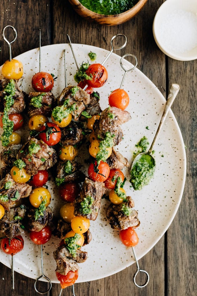 A platter of grilled flank steak skewers drizzled with paleo parsley pesto on a wood table.