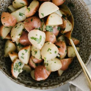 No mayo italian potato salad in a brown ceramic bowl, dressed with red wine vinaigrette, parsley, and chives.