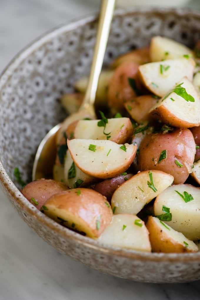 Italian potato salad with red wine vinaigrette, parsley, and chives in a brown serving bowl with a gold serving spoon.