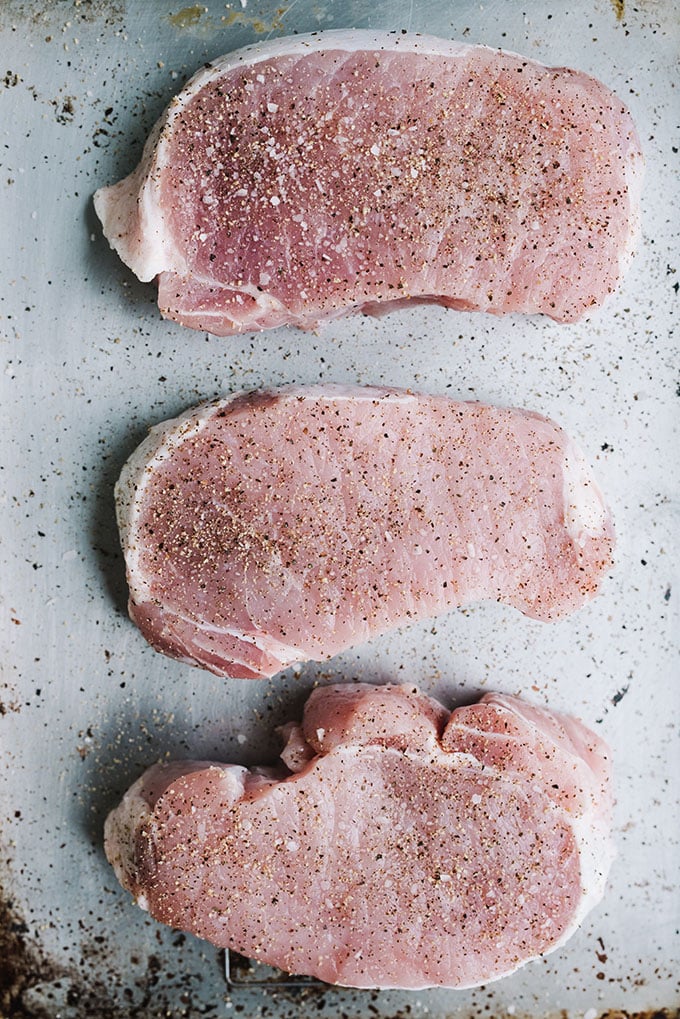 Raw thick cup pork chops seasoned with salt and pepper on a baking sheet.