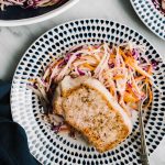 Tender thick cut oven roasted pork chops over apple jicama slaw on a blue and white plate with a navy linen napkin.