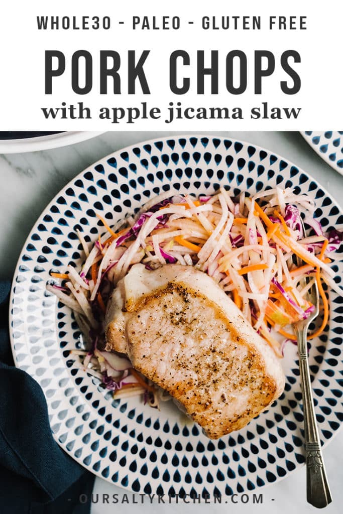 Tender thick cut oven roasted pork chops over apple jicama slaw on a blue and white plate with a navy linen napkin.