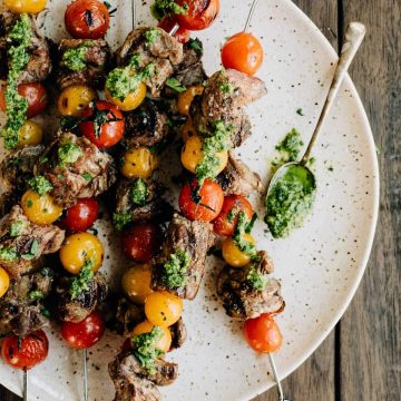 A platter of tomato and steak skewers drizzled with dairy free pesto on a wood background.
