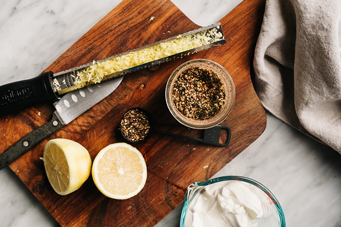 Zaatar chicken ingredients - lemon juice, lemon zest, yogurt, and zaatar spice - on a cutting board.