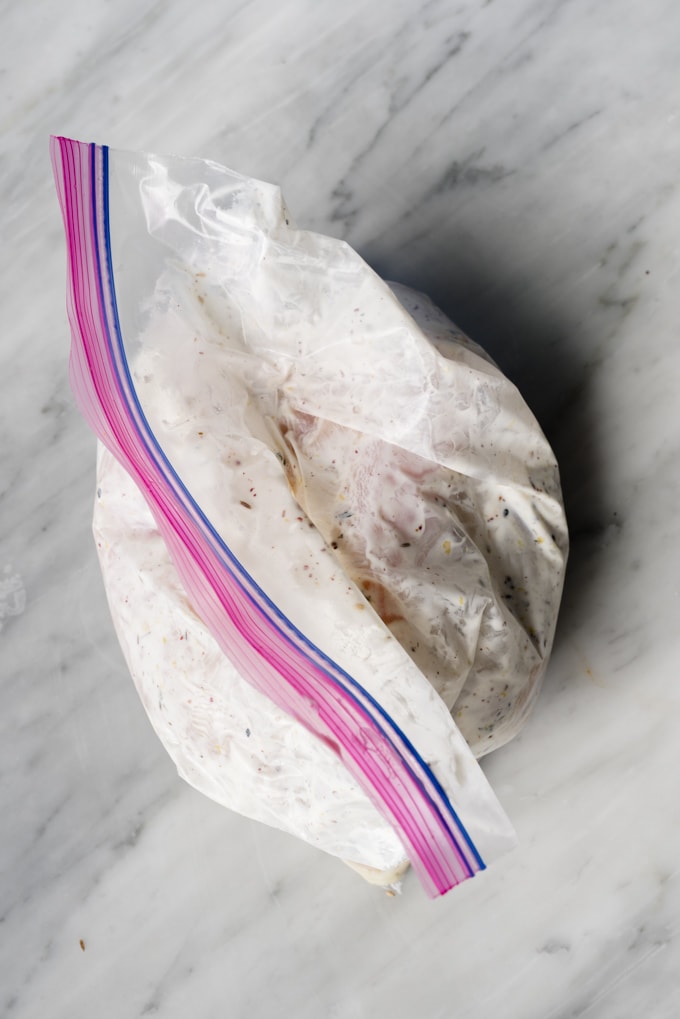 Raw chicken breasts marinated with yogurt, lemon, and zaatar spice in a gallon sized ziplock bag.
