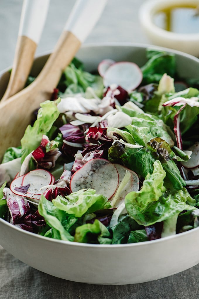 A tossed green salad in a bowl with butter lettuce, radicchio, fennel, and radishes.