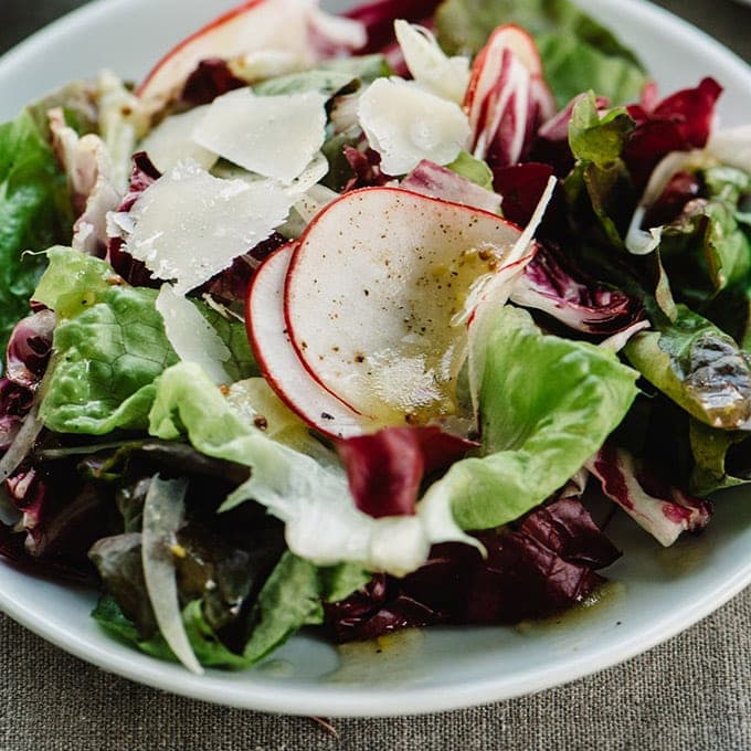 Butter lettuce and radicchio tossed salad on a small white plate drizzled with champagne vinaigrette.