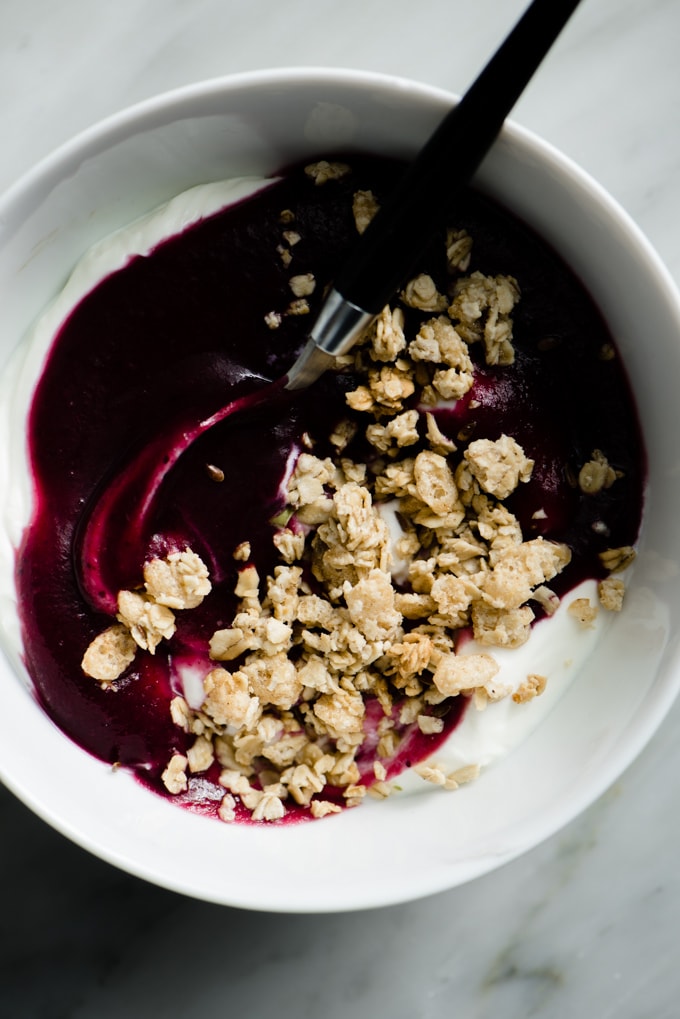 A bowl of greek yogurt topped with blueberry applesauce and granola.