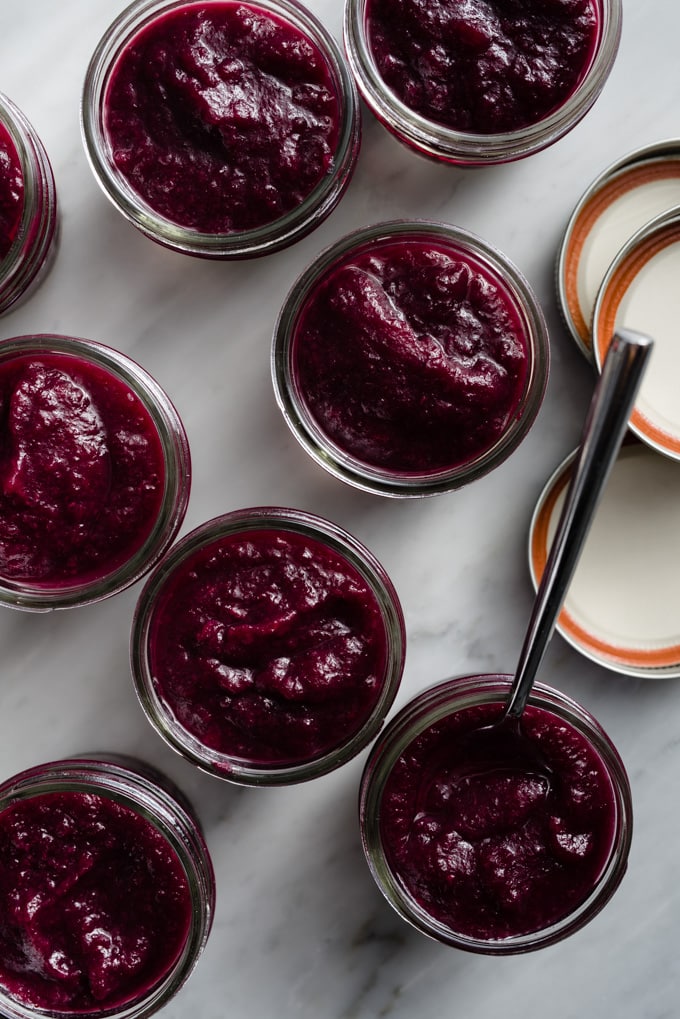 Several small jars of chunky blueberry applesauce on a marble table.