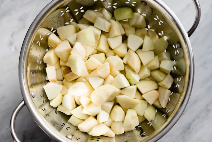 Peeled, diced apples in a colander for making homemade blueberry applesauce.