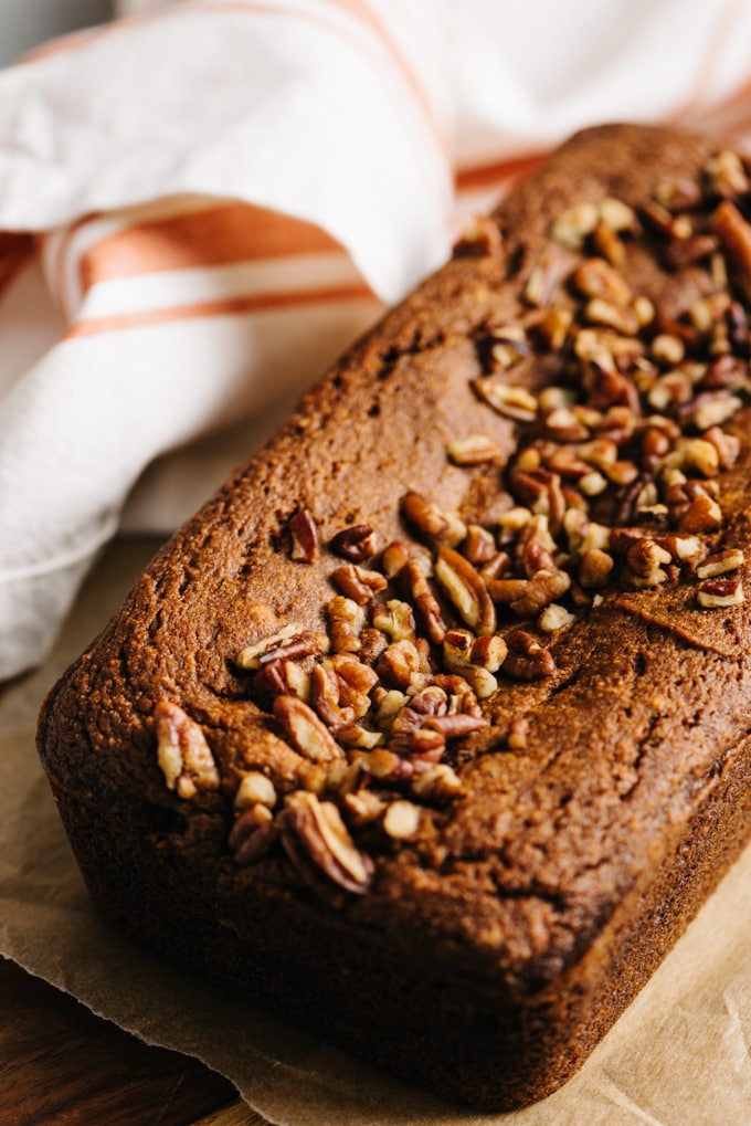 A loaf of paleo pumpkin bread topped with pecans on a cutting board.