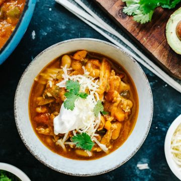 A bowl of gluten free pumpkin chicken chili on a black surface surrounded by small bowls of toppings.