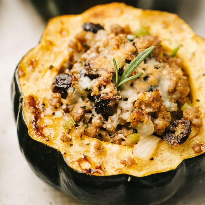 Side view, sausage stuffed acorn squash on a parchment lined baking sheet.