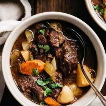 A bowl of red wine beef stew with a soup spoon and fresh parsley garnish.