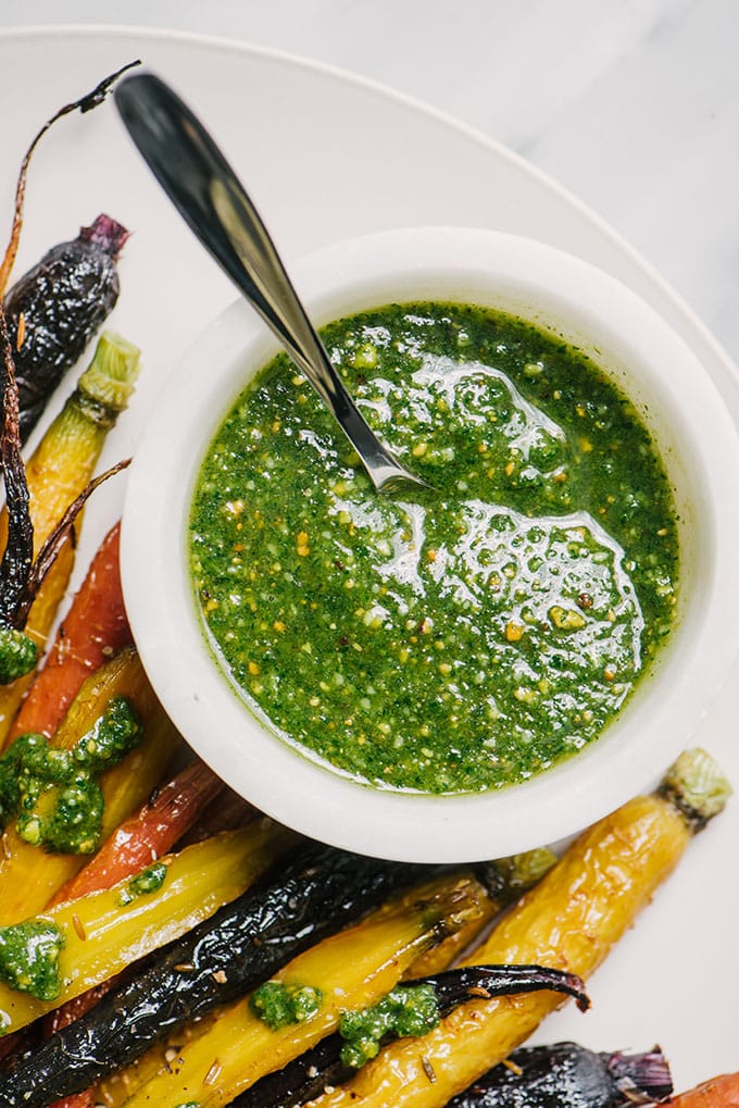 Carrot green pesto in a white marble bowl on a platter surrounded with honey roasted carrots.